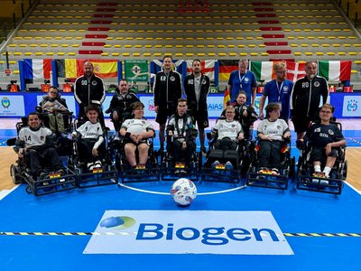 Auf der Fotografie ist die deutsche Nationalmannschaft im E-Rollstuhl Fußball in der Halle in Lignano Sabbiadoro zu sehen. Die Spieler befinden sich mitsamt ihren Rollstühlenstühlen in der ersten Reihe, die Trainer reihen sich dahinter ein. Vor allen liegt ein Ball in der Mitte des Bildes. Foto: Agentur Frontcourt