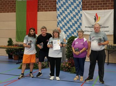 Auf dem Bild ist das fünfköpfige Team der SV Rhinos in der Austragungshalle zu sehen. Alle lächeln in die Kamera und zeigen Ihre Urkunden/Präsente in die Kamera.