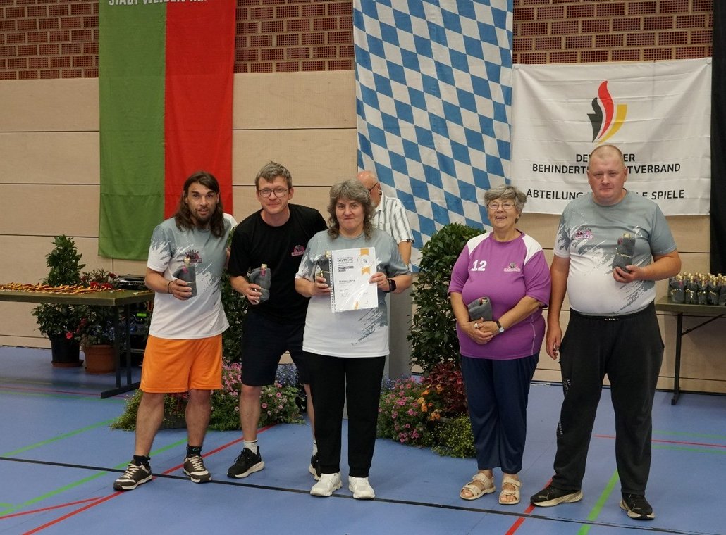 Auf dem Bild ist das fünfköpfige Team der SV Rhinos in der Austragungshalle zu sehen. Alle lächeln in die Kamera und zeigen Ihre Urkunden/Präsente in die Kamera.