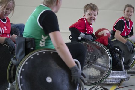 Kinder sitzen in Rugbyrollstühlen und spielen Rollstuhlrugby