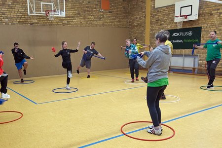 Teilnehmende stehen in der Sporthalle in Gymnastikreifen.