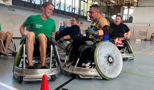 Mehrer Männer sitzen in Rugbyrollstühlen und spielen Rollstuhlrugby.